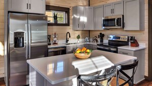 A modern kitchen with stainless steel appliances, grey cabinets, and a central island with a bowl of fruit. - Fab New 2 Level Build I Fire Pit I Private Hot Tub I Game Room (Sevierville)