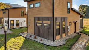 Ein modernes, zweistöckiges Haus mit einer braunen Fassade, großen Fenstern und einem Kiesweg, der zum Eingang führt.