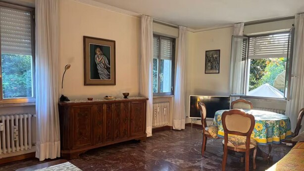 Zona pranzo con un armadio in legno, due sedie, un tavolo con tovaglia floreale e un quadro appeso al muro.