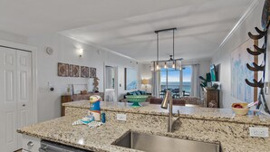 Cozinha com bancadas de granito, eletrodomésticos de aço inoxidável e vista para a sala de estar.