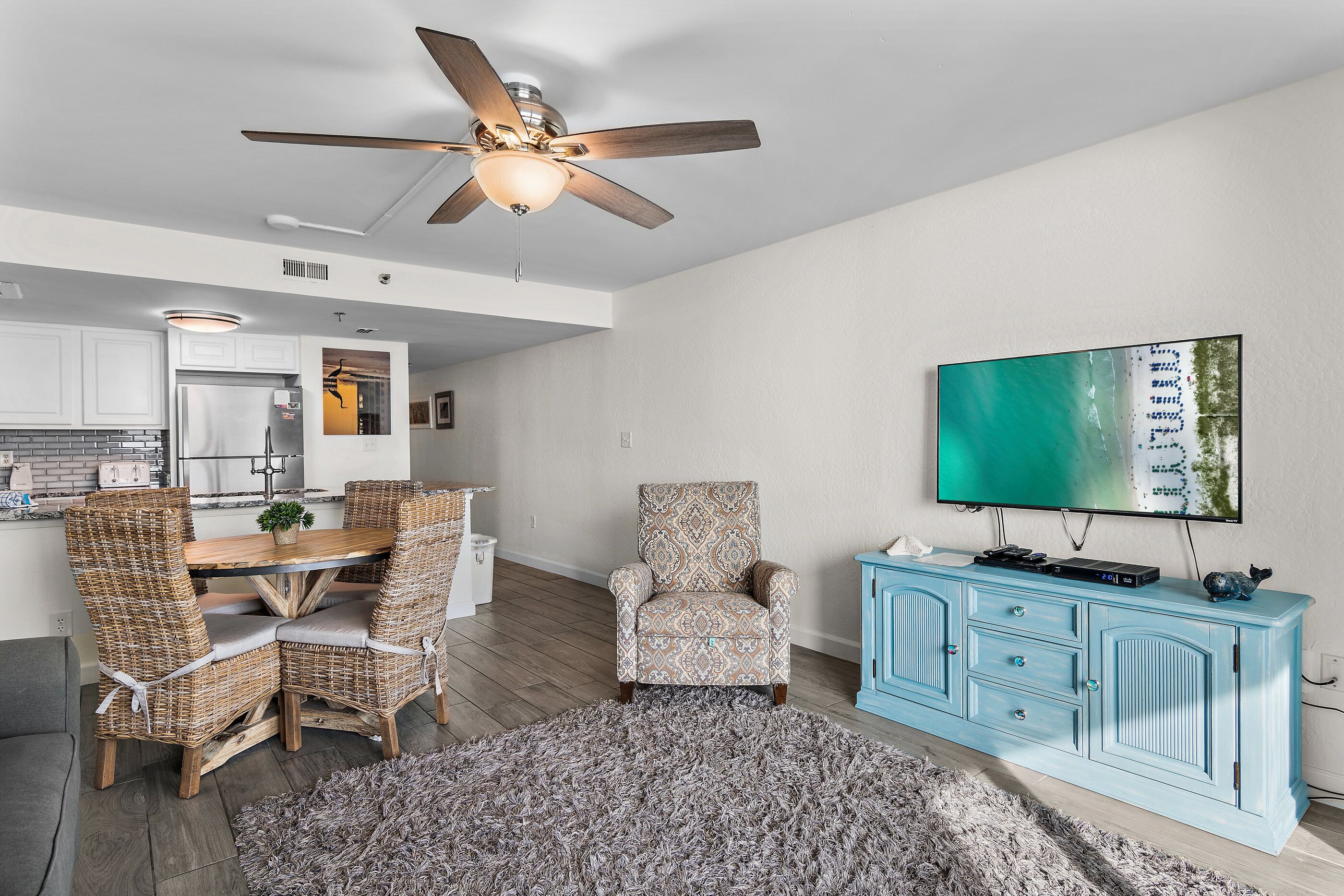 A modern living room with a dining area, a ceiling fan, a flat-screen TV, and a light blue cabinet.