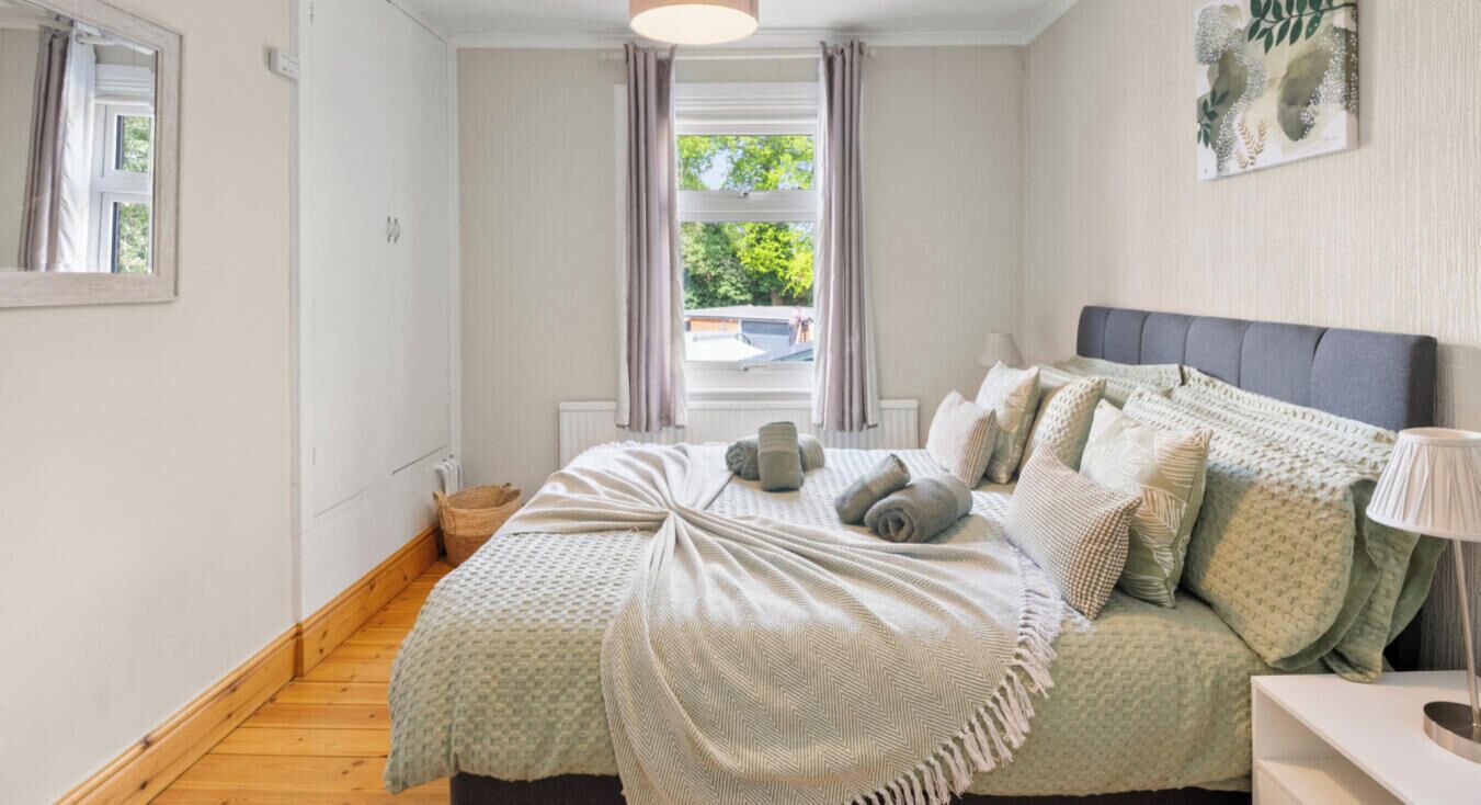 A bedroom with a bed, a bedside table, a lamp, and a window with curtains.