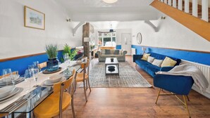 A dining area with a table set for four, a blue sofa, and a staircase. - Heartwarming Windsor Cottage with Free Parking (Berkshire)