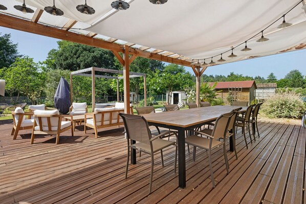 An outdoor patio with a wooden deck, a covered seating area, and a dining table with chairs.