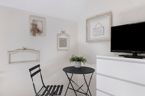 A room with a white desk, a black chair, a television, and wall-mounted decorations including a teddy bear and framed pictures.