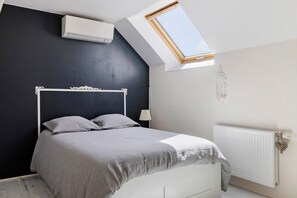 A bedroom with a skylight, a white bed, and a radiator.