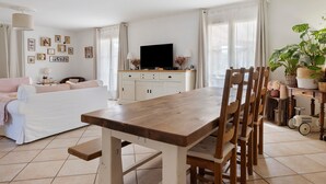 Un salon avec une table à manger en bois, un canapé blanc et un téléviseur posé sur un meuble.