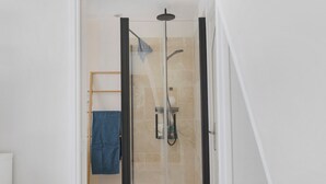 Une douche fermée par des parois en verre, dotée d’un pommeau de douche à main et d’un porte-serviettes avec une serviette bleue.