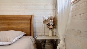 Un lit en bois avec un oreiller blanc, une table de chevet avec une lampe et un vase décoratif contenant des fleurs séchées.