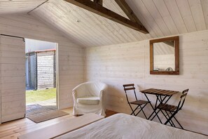 Una habitación con techo de madera, una silla blanca, una pequeña mesa de madera y un espejo en la pared.