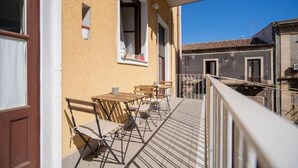 Un balcón con mobiliario exterior, una ventana con cortina y vistas a edificios vecinos.