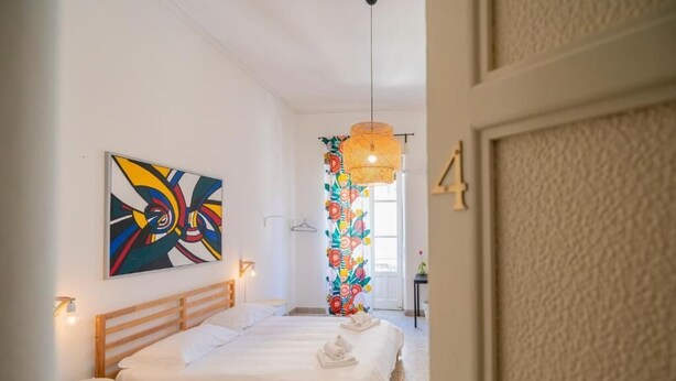 Una habitación de hotel con una cama grande, un cuadro abstracto de colores y una lámpara colgante decorativa.