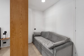 A modern room with a grey sofa, a wooden door, and a small table with a lamp. - Room 'Camera 2 - P2' with Balcony, Wi-Fi, and Air Conditioning (Balestrate)