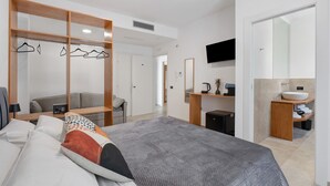 A modern hotel room with a bed, a seating area, a TV, a bathroom with a sink and mirror, and a wardrobe with clothes hanging. - Room 'Camera 2 - P2' with Balcony, Wi-Fi, and Air Conditioning (Balestrate)
