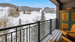 A balcony with a view of a snowy landscape, a wooden chair, and a cabinet. - Highlands Slopeside 502 (Beaver Creek)