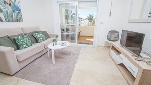 Een woonkamer met een bank, salontafel, televisie en uitzicht op een balkon.