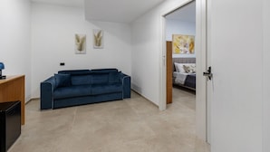 A modern room with a blue sofa, a wooden desk, and a bed with a white headboard. - Room 'Camera 3 - P1 Con Accesso Disabili' with Balcony, Wi-Fi and Air Conditioning (Balestrate)