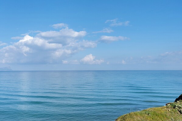 Eine Küstenlandschaft mit ruhiger See, blauem Himmel und weiter Küste im Hintergrund.