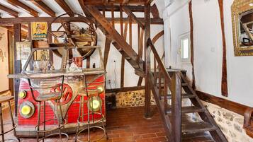 Un intérieur rustique avec des poutres apparentes, un escalier et une table rouge accompagnée de tabourets.