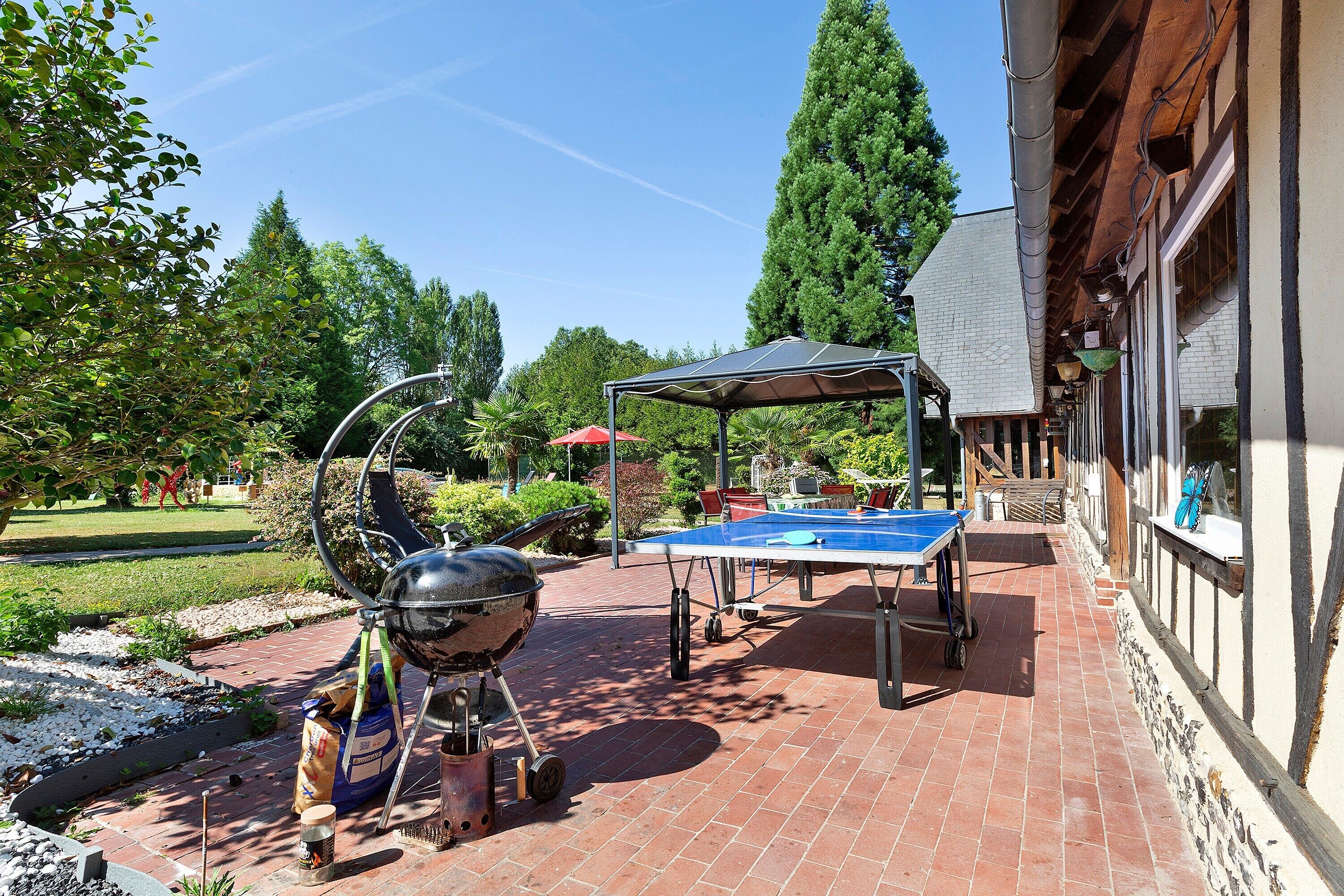 Une terrasse extérieure équipée d’un barbecue, d’une table de ping-pong et d’un espace salon abrité.