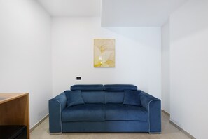 Une pièce moderne avec un canapé bleu, un bureau en bois et un tableau abstrait accroché au mur.