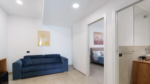 A modern room with a blue sofa, a wooden cabinet, and a bed in the background. - Room 'Camera 3 - P2' with Balcony, Wi-Fi and Air Conditioning (Balestrate)