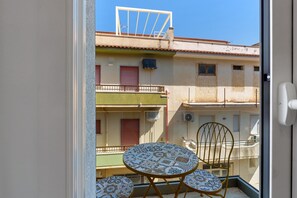 Un balcon avec une table et des chaises, une vue sur les bâtiments voisins et un ciel dégagé.