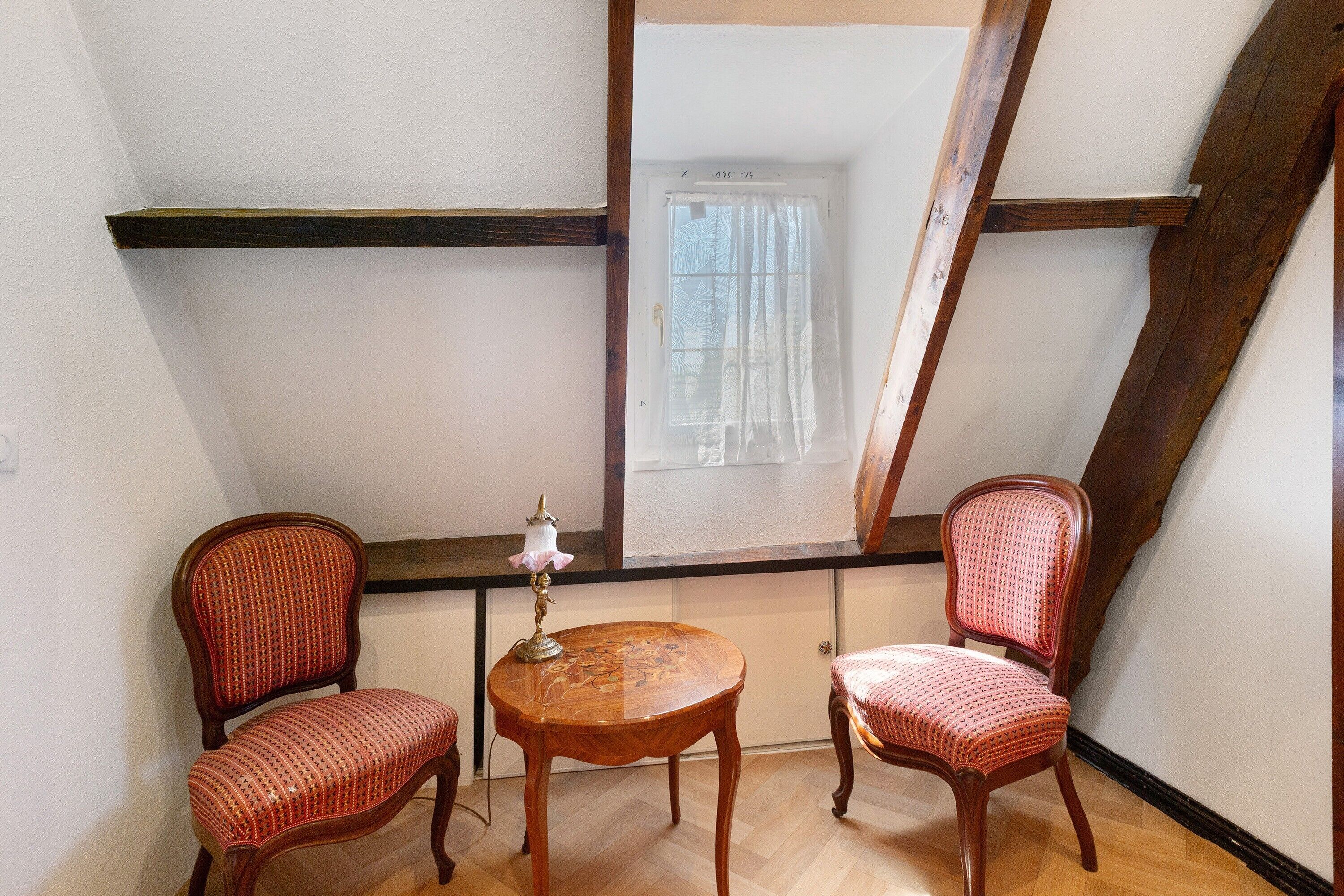 A room with two wooden chairs, a small round table, and a window with a curtain.