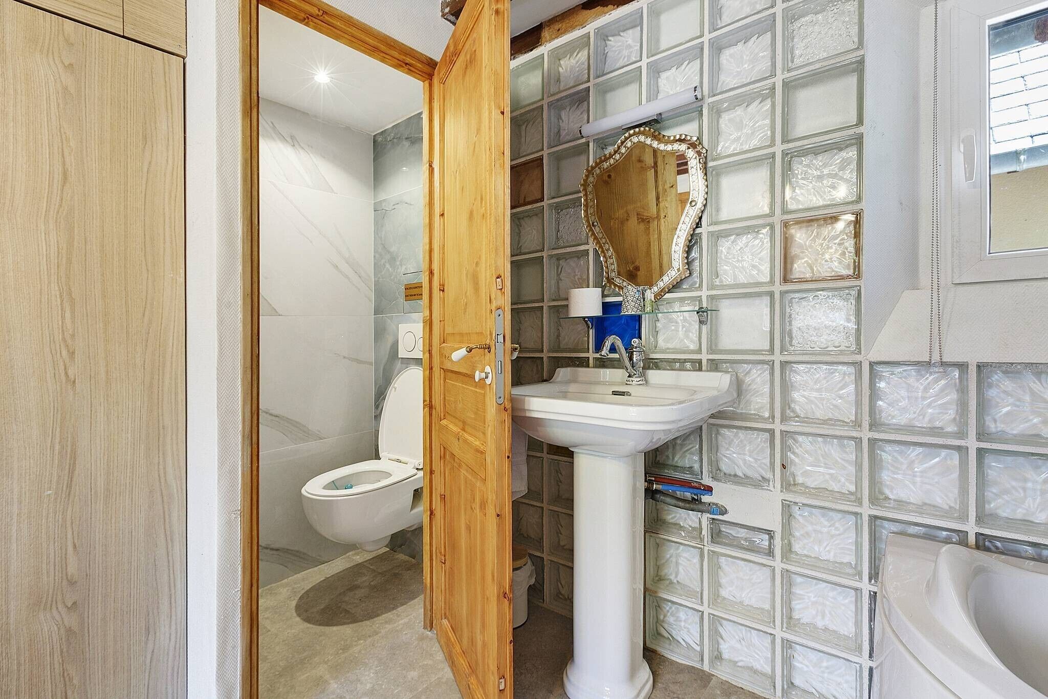 A bathroom with a wooden door, a white sink, a mirror, and a toilet.