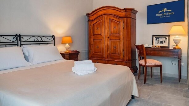 A hotel room with a bed, a wooden wardrobe, a desk with a chair, and a framed picture on the wall. - Palazzo dei Pavoni Relais di Charme (L'Aquila)