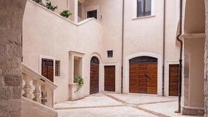 A courtyard with a stone floor, a staircase, and a wooden door. - Palazzo dei Pavoni Relais di Charme (L'Aquila)