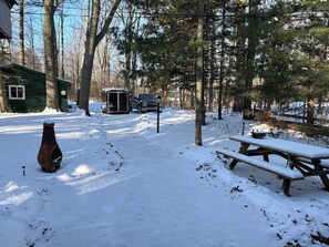 A snowy outdoor area with a green cabin, a black truck, and a picnic table.
