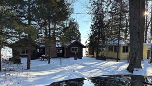 A cabin with a snow-covered yard, surrounded by trees.