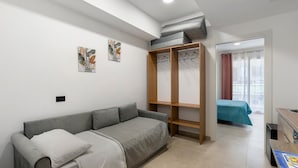 A modern room with a grey sofa, a wooden wardrobe, a bed with a teal bedspread, and a small kitchenette. - Apartment 'Mini - P1' with Balcony, Wi-Fi and Air Conditioning (Balestrate)