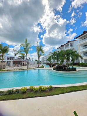 A swimming pool with lounge chairs, palm trees, and a building with balconies. - Cefiro 101 Garden Breeze • 10-Min Walk to Playa Dominicus (Dominicus)