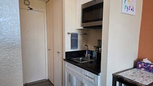 Cozinha compacta com armários brancos, bancada preta, micro-ondas e pia.