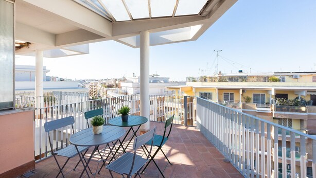 A balcony with a glass roof, white railing, and a table with chairs. - Rental in Rome Aurelia Sunset Penthouse (Rome)
