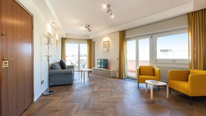 A spacious living room with a sofa, yellow armchairs, a coffee table, and a TV on a stand. - Rental in Rome Aurelia Sunset Penthouse (Rome)