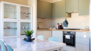 A modern kitchen with white and green cabinets, a marble countertop, and a dining area with a table and chairs. - Rental in Rome Aurelia Sunset Penthouse (Rome)