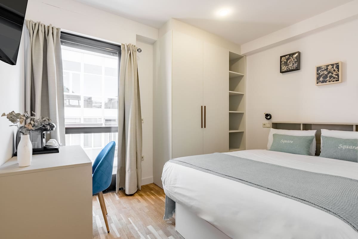 A bedroom with a bed, a desk, a chair, and a window with curtains.