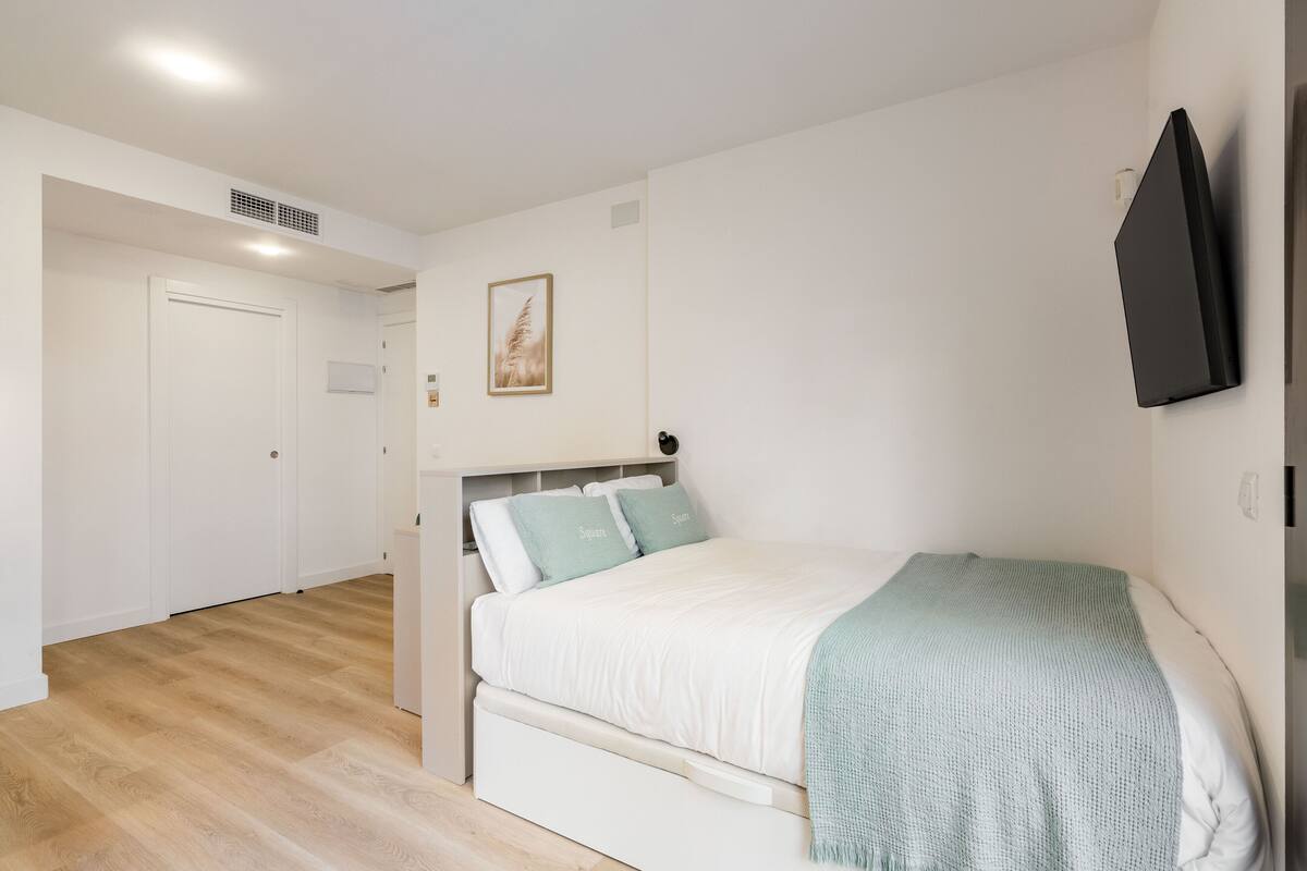 A bedroom with a bed, a wardrobe, a flat-screen TV, and a framed picture on the wall.