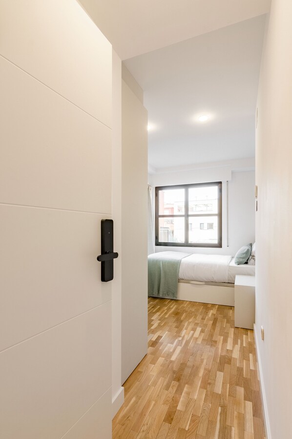 A narrow hallway with a wooden floor leading to a bedroom with a window and a bed. - Square Rooms by Charming (Madrid)