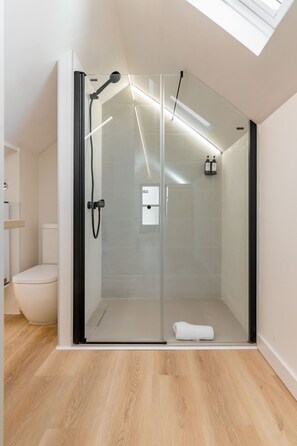 A modern shower room with a glass door, a white toilet, and a wooden floor. - Square Rooms by Charming (Madrid)