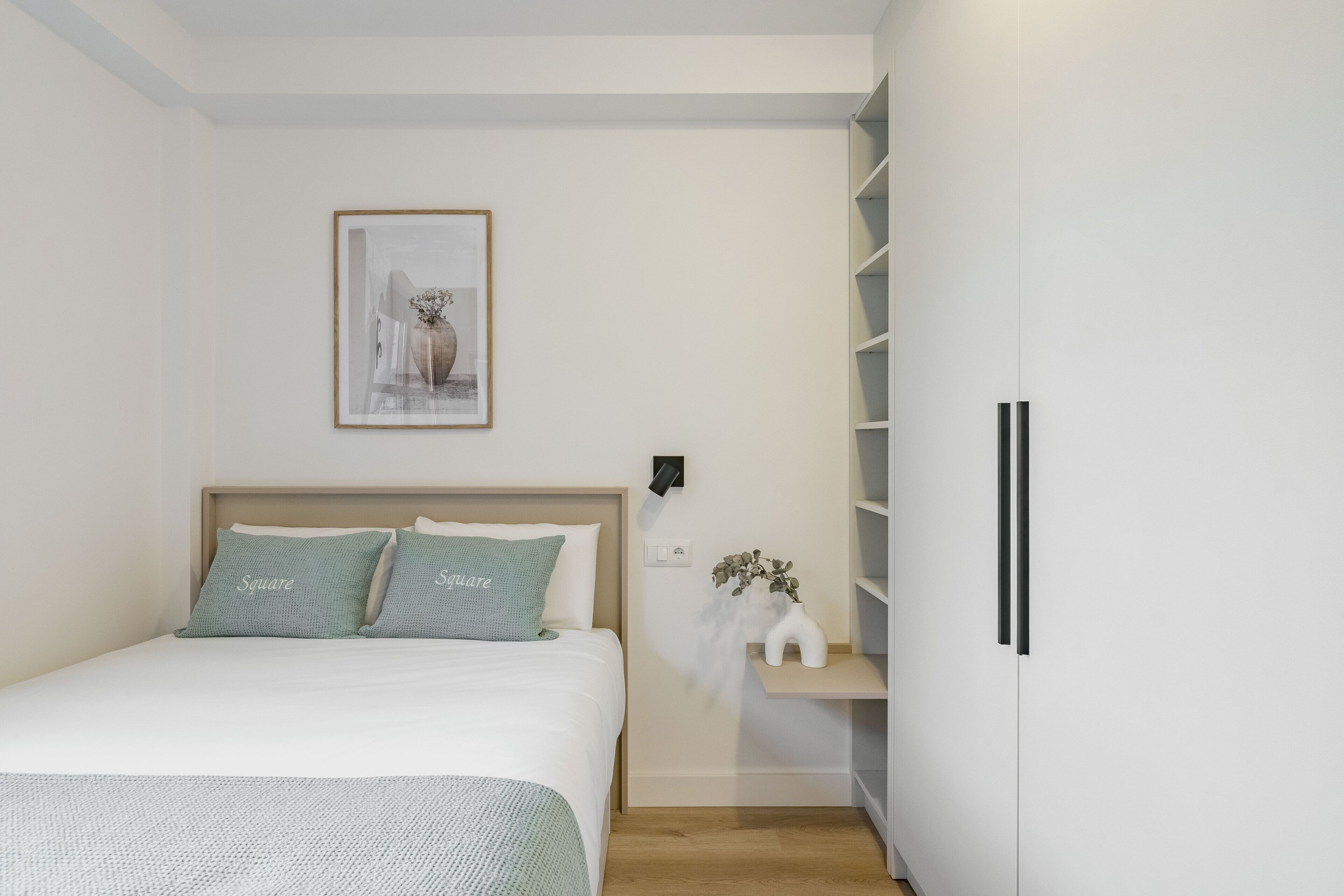Une chambre à coucher avec un lit, une table de chevet ornée d’un vase et une armoire.