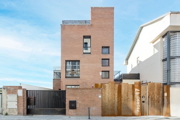 A multi-story building with a brick facade, a gated entrance, and a clear sky. - Square Rooms by Charming (Madrid)