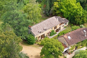 A two-story stone building with a tiled roof, surrounded by dense greenery.