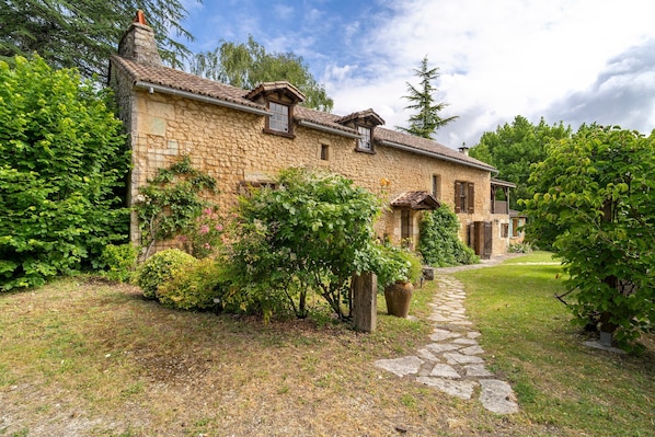 A stone house with a stone pathway leading to the entrance, surrounded by greenery.