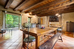 Un comedor rústico con una mesa de madera, bancos y sillas, una pared de piedra y vistas a través de un ventanal.