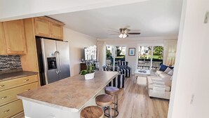 Una cocina moderna con una isla central, taburetes de bar y un comedor con sofá y sillas.
