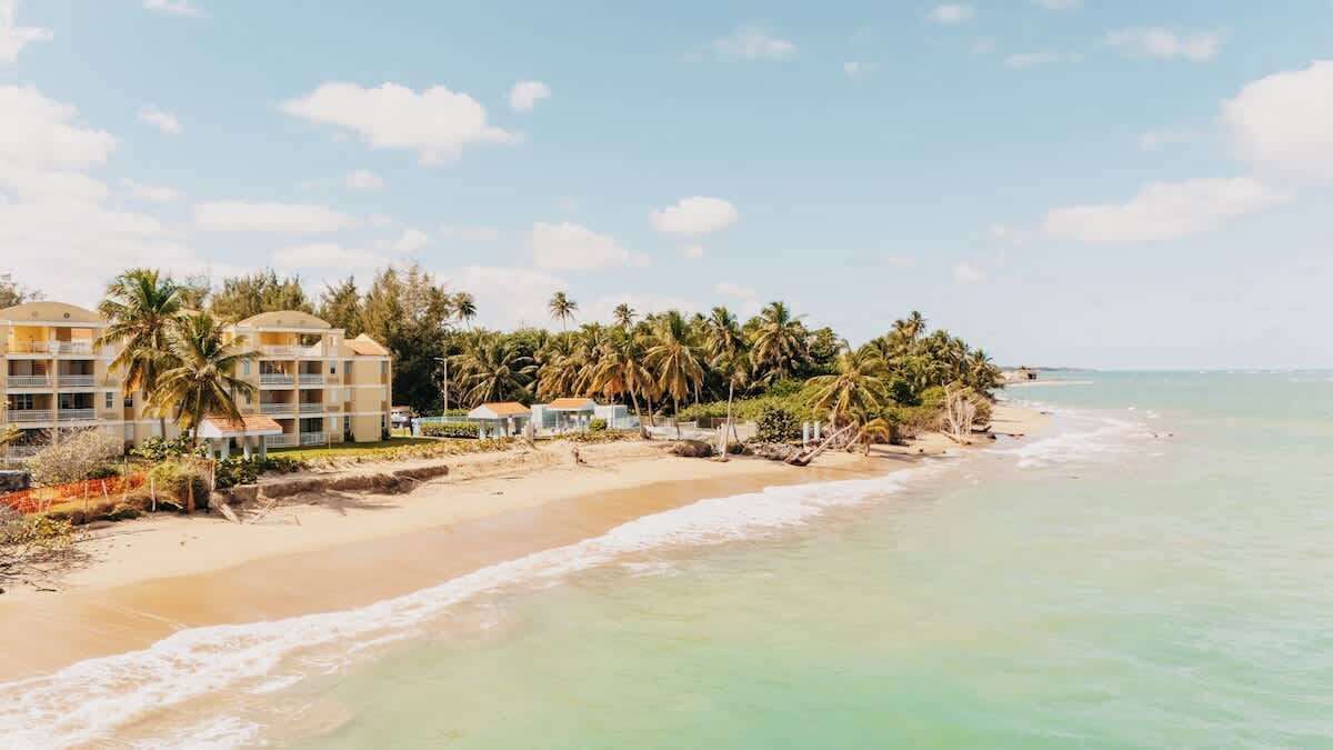 A beachfront hotel with multiple balconies, palm trees, and a sandy beach.